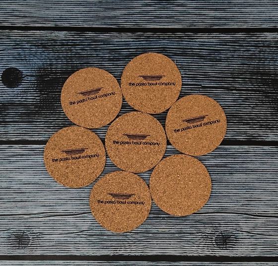 Cork coasters with printed bowl logo, seven on dark wood, custom made by RestroCart, New Delhi