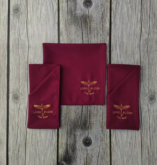 Maroon table napkins with gold embroidered logo, three pieces, custom made by RestroCart, New Delhi